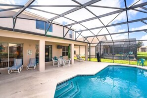 A covered outdoor swimming pool area with lounge chairs and a glass-enclosed structure.