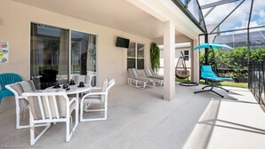 A covered patio with white furniture, a hanging chair, and a blue umbrella. - Emerald Island - 7bd/4.5ba Pool Home - #7ei565 (Kissimmee)