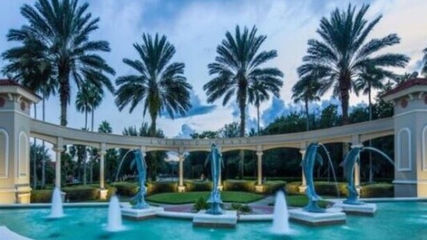 A pool area with multiple fountains, surrounded by palm trees and a covered walkway. - Emerald Island - 7bd/4.5ba Pool Home - #7ei565 (Kissimmee)