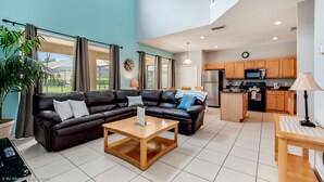 A spacious living area with a black leather sofa, a wooden coffee table, and a view of the kitchen in the background. - Emerald Island - 7bd/4.5ba Pool Home - #7ei565 (Kissimmee)