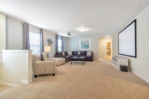 A living room with a sectional sofa, a coffee table, and a flat-screen TV mounted on the wall.