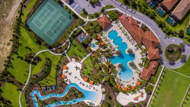 Eine Vogelperspektive auf ein Resort mit einem großen zentralen Pool, einem Tennisplatz und einem gewundenen Wasserspiel.