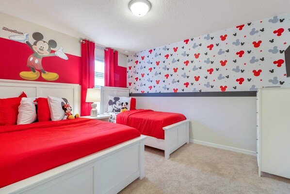 A bedroom with two beds, red bedding, and Mickey Mouse-themed decor.