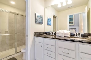 A modern bathroom with a glass shower enclosure, a large mirror, and a granite countertop with a sink and towel rack.