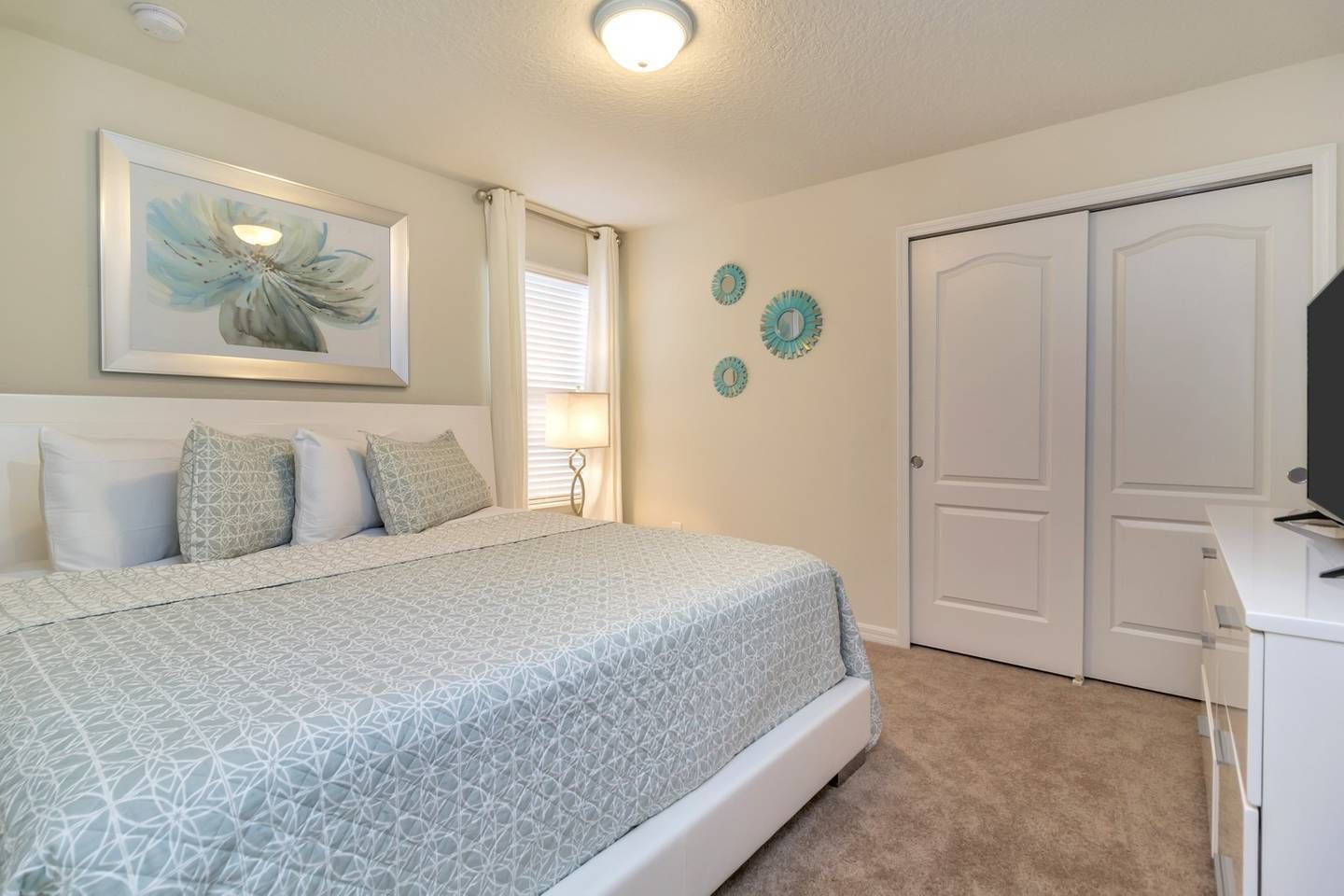 A bedroom with a bed, a desk, a television, and a door.