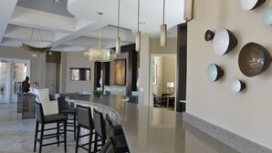 A modern kitchen with a curved island, bar seating, pendant lighting, and a wall-mounted light fixture.