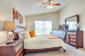 A bedroom with a bed, a dresser, a vanity, a ceiling fan, and artwork on the walls.