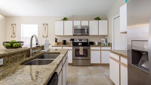A modern kitchen with granite countertops, stainless steel appliances, and white cabinetry. - Hampton Lakes - Spacious 4bd/2ba Pool Home #4hl510 (Davenport)
