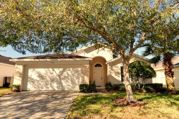 A single-story house with a covered driveway, a front door, and a large tree in front.
