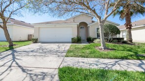 A single-story house with a garage, a front lawn, and a tree. - Hampton Lakes - Spacious 4bd/2ba Pool Home #4hl510 (Davenport)