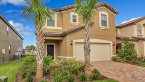 A two-story house with a beige exterior, a garage, and a well-maintained front yard with palm trees and shrubs. - Solterra Resort 7BD Brand New Pool Home #7st565 (Davenport)