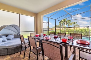 A sunroom with a glass ceiling, a dining table set with red bowls and glasses, and a cushioned seating area with a canopy. - Solterra Resort 7BD Brand New Pool Home #7st565 (Davenport)