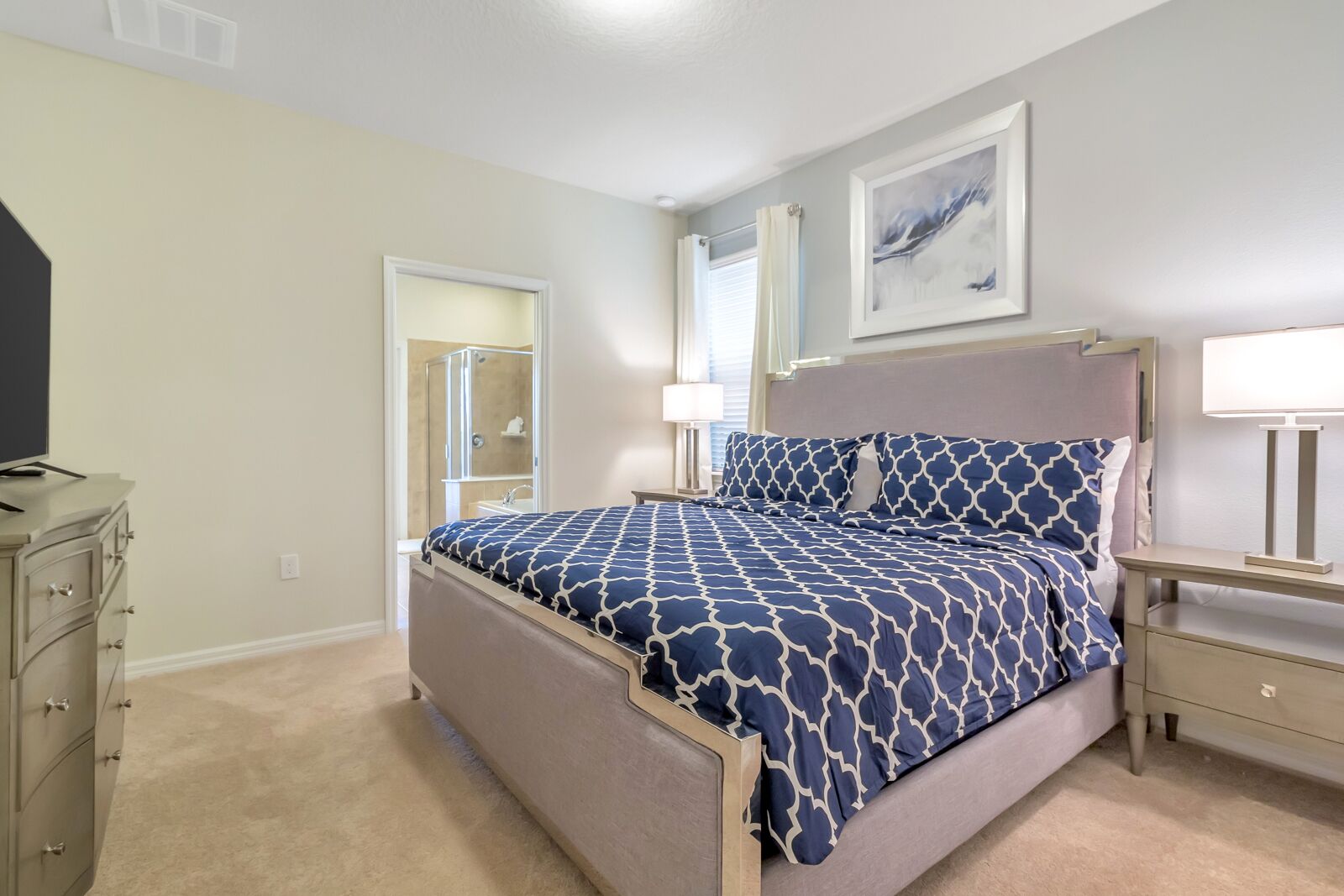 A bedroom with a bed, bedside tables, a dresser, a shower, and a painting on the wall.