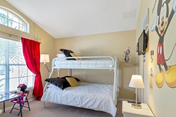 Habitación con literas, una ventana, cortinas rojas, un escritorio con silla y decoración de Mickey Mouse.