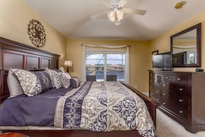 A bedroom with a bed, dresser, TV, and a view of a balcony.