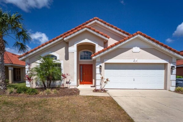 A two-story house with a red-tiled roof, a garage, and a well-maintained front yard with palm trees and shrubs.