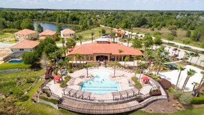 An aerial view of a resort with a central swimming pool, surrounding lounge areas, and multiple buildings with red-tiled roofs.