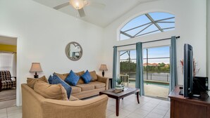 A spacious living room with a large sofa, two lamps, a coffee table, and a TV.