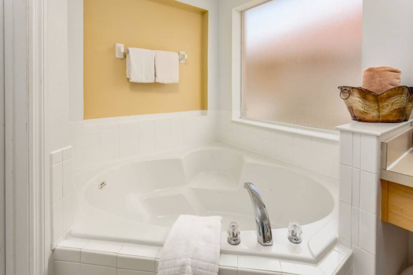 A bathroom with a large bathtub, a towel rack with two towels, and a window with a frosted glass view.