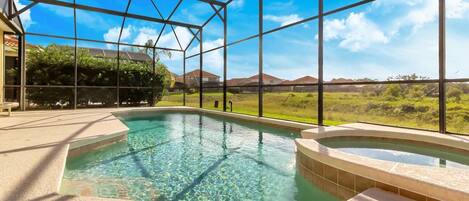 An indoor swimming pool with clear water, surrounded by a glass enclosure, and a view of a suburban landscape.