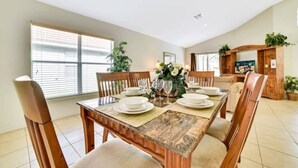 A dining room with a wooden table set for four, surrounded by chairs, with a television and plants in the background. - Aviana - Pet Friendly 4bd/3ba Pool Home - #4av136 (Davenport)