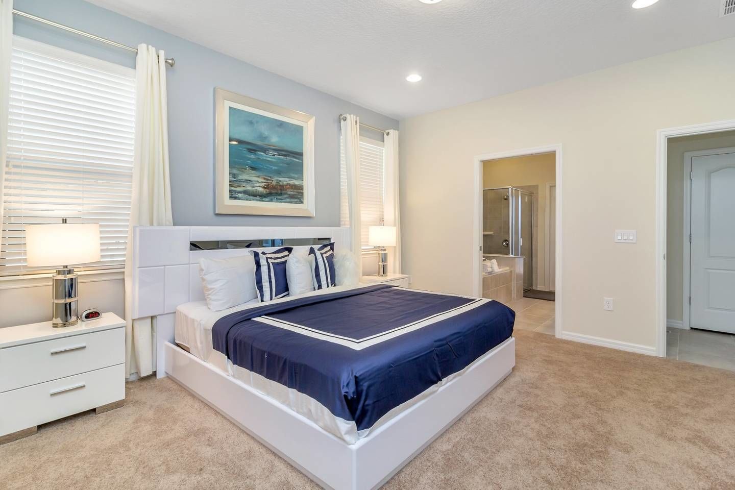 A bedroom with a bed, bedside tables, a painting, and a bathroom door.
