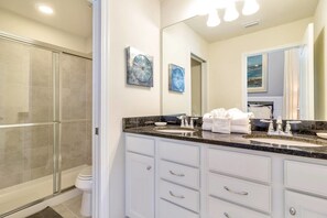 A modern bathroom with a glass shower enclosure, a large mirror, and a granite countertop with a sink and towel rack.