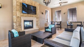 A spacious living area with a fireplace, comfortable seating, and a television mounted on a stone wall. - Brand New Luxurious Pool Home in Westside! 5bd/4ba #5ws690 (Kissimmee)