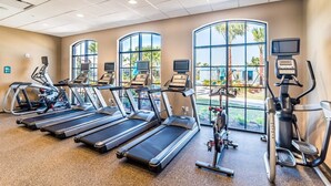 A gym with treadmills, elliptical machines, and a stationary bike, large windows with a view of greenery, and a ceiling with recessed lighting. - Brand New Luxurious Pool Home in Westside! 5bd/4ba #5ws690 (Kissimmee)