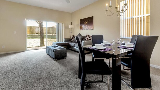 A dining area with a table set for four, a sofa, and a large window with blinds.