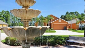 A fountain with multiple tiers in a landscaped area with a house in the background. - Watersong - Luxurious 5bd/4.5ba Pool Home #5wr510 (Davenport)