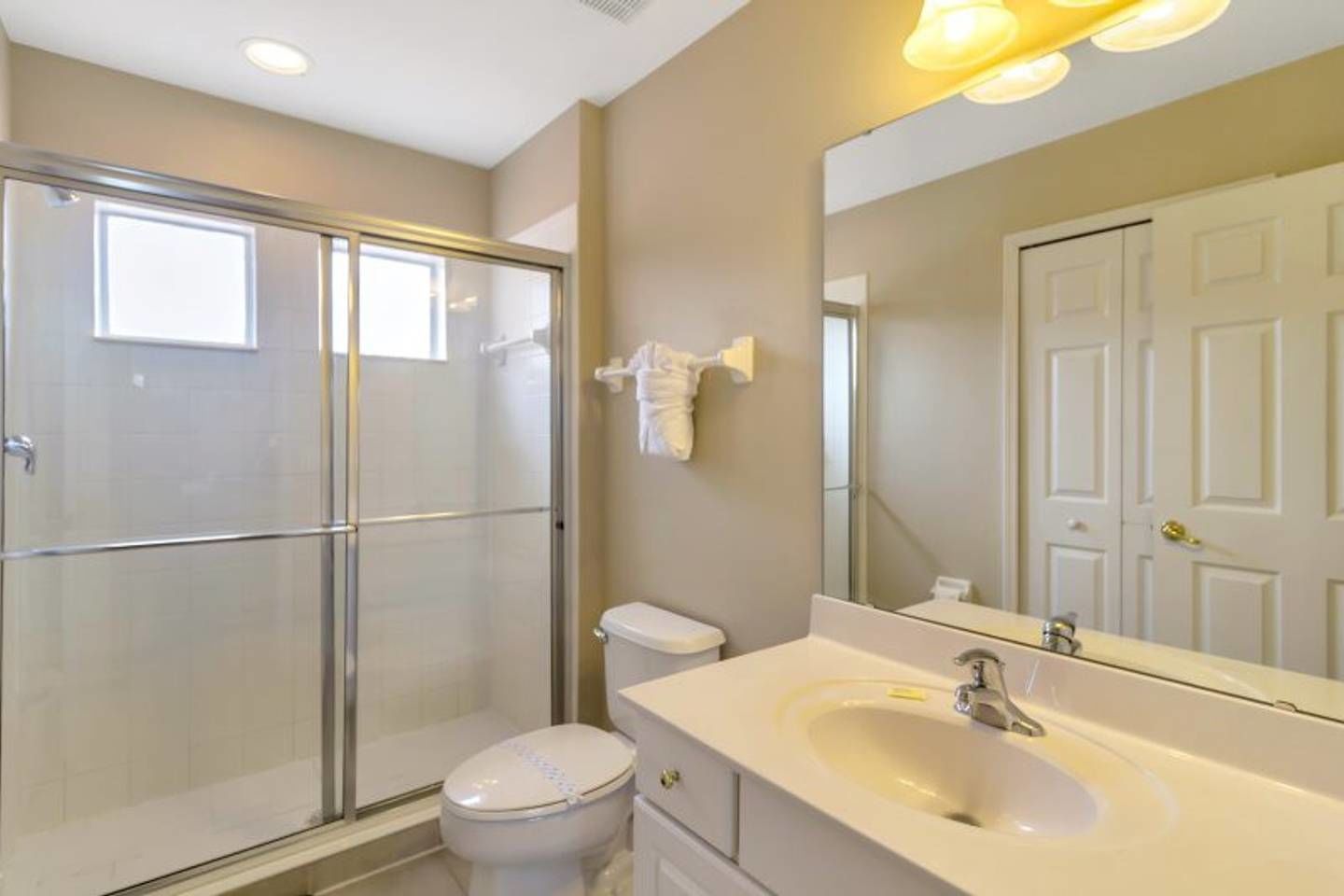 A bathroom with a glass shower enclosure, a toilet, and a sink with a mirror above it.