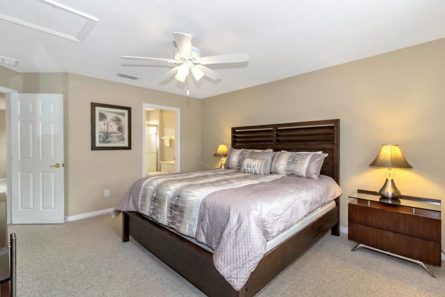 A bedroom with a bed, bedside lamps, a ceiling fan, and a door.