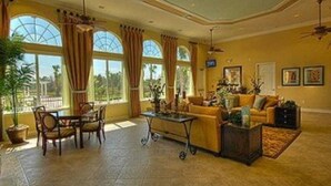 A spacious living room with a large window, a dining area with a table and chairs, and a sofa set. - Watersong - Luxurious 5bd/4.5ba Pool Home #5wr510 (Davenport)