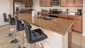 A kitchen with granite countertops, stainless steel appliances, and wooden cabinets. There are four bar stools with chrome bases. - Marbella South - Lovely 5bd/3.5ba PH #5ms040 (Davenport)