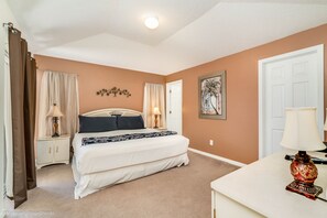 A bedroom with a double bed, two bedside tables with lamps, a door, and a wall-mounted artwork.