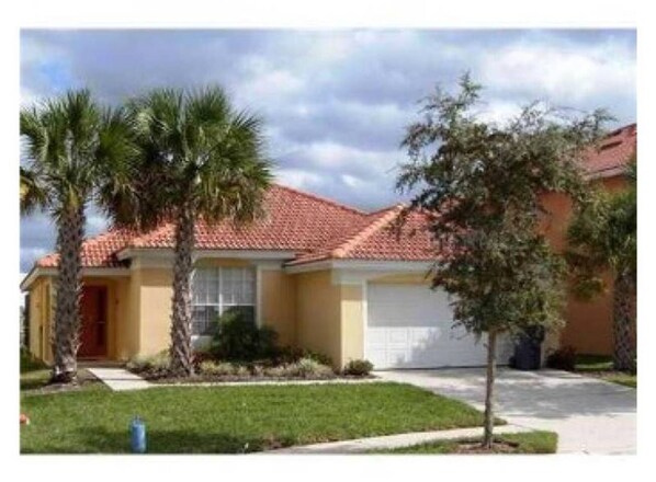 A single-story house with a red-tiled roof, a front garage, and a well-maintained lawn with palm trees.
