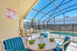 A covered outdoor area with a pool, lounge chairs, and a table with green bowls and a white water bottle.