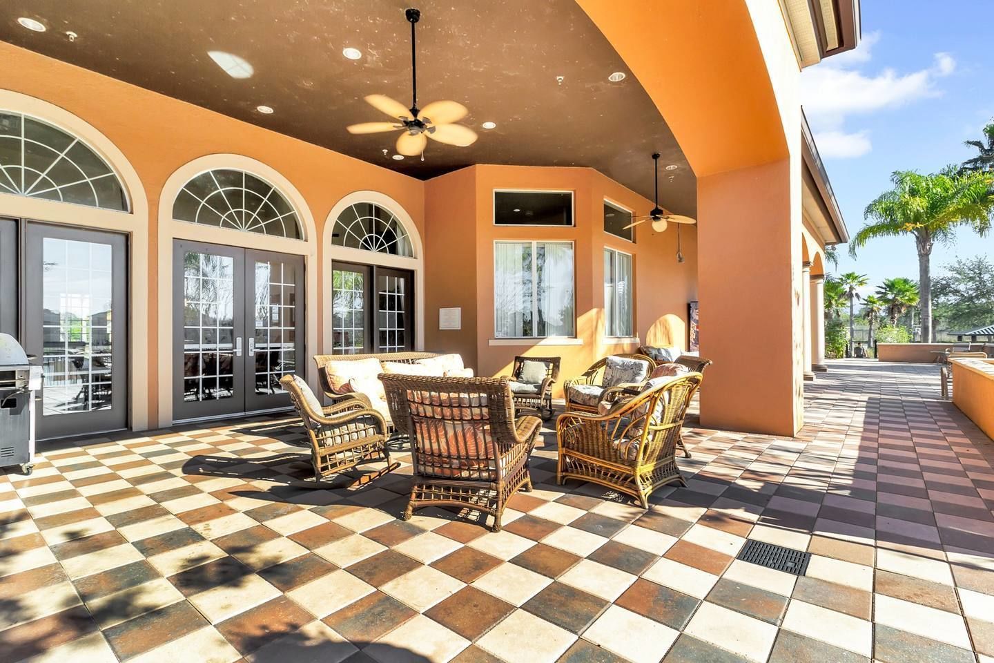 A covered patio with checkered flooring, wicker furniture, and a ceiling fan.