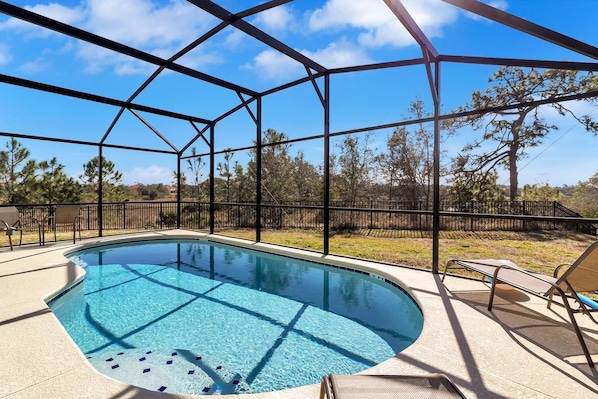 A covered swimming pool with a clear blue water feature, surrounded by a metal fence and trees in the background.