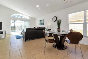 A modern living room with a sofa, a dining table with chairs, a TV, and a large window.