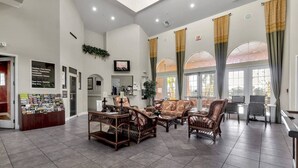 A spacious lobby with a reception desk, seating area with wicker furniture, and large windows with curtains.