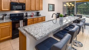 Una cocina moderna con armarios de madera, encimeras de granito, estufa integrada y una zona de bar con asientos.