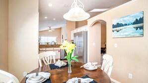 Un coin repas avec une table en bois, des chaises blanches, un vase rempli de fleurs jaunes et, au fond, une cuisine moderne.