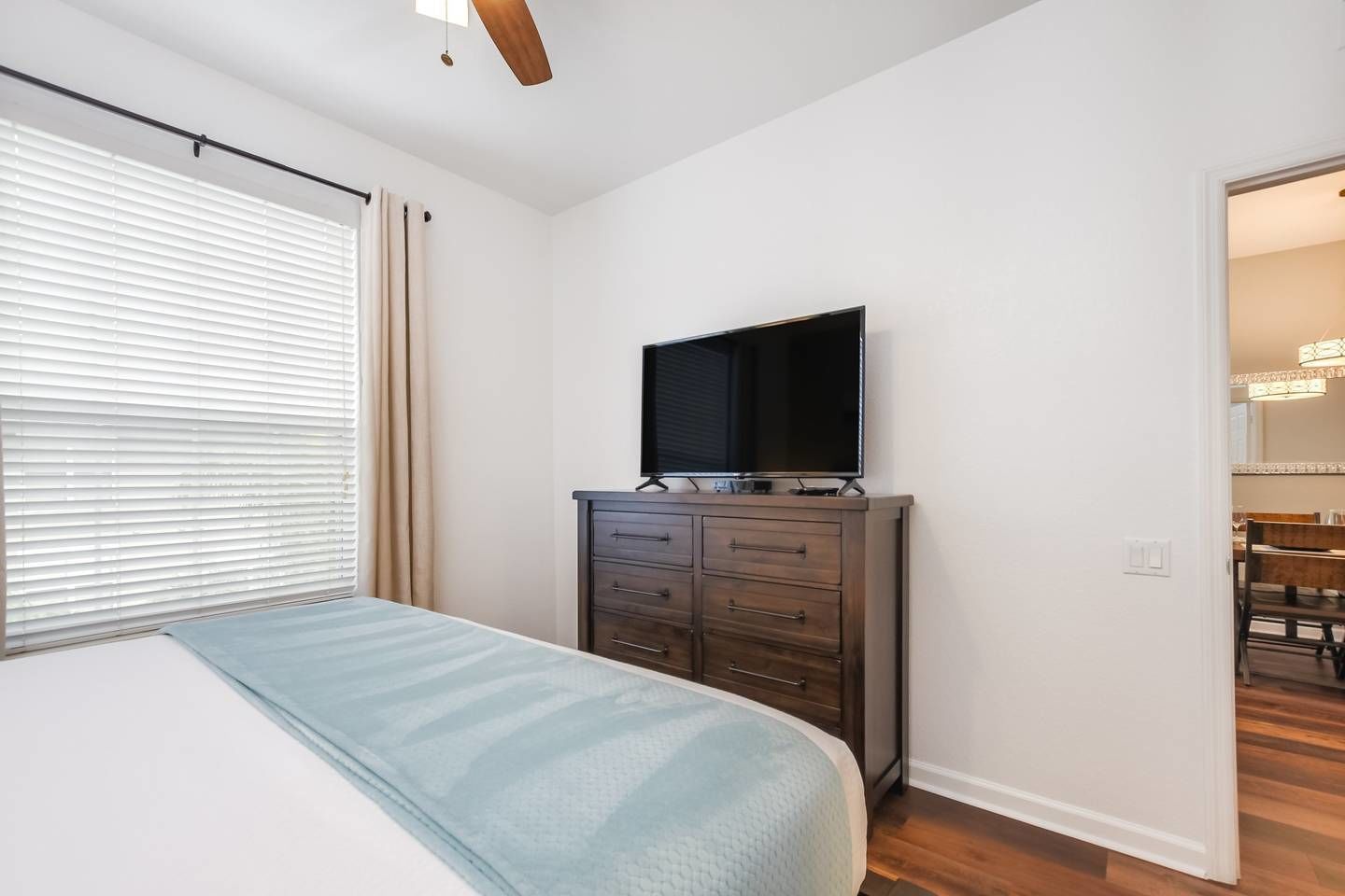 Un dormitorio con cama, cómoda, televisor y puerta que da a un comedor.