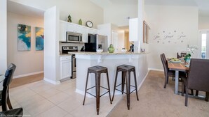 Une cuisine moderne avec des meubles blancs, un îlot central doté de tabourets et un coin repas avec une table et des chaises.