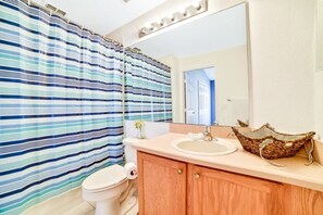 Une salle de bain avec des rideaux de douche à rayures, des toilettes, un lavabo avec un panier en osier et un miroir.