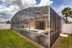 A covered outdoor area with a pool, enclosed by a metal screen, and a patio with chairs. - Hampton Lakes - Lovely 4bd/3ba Pool Home 4hl904 (Davenport)