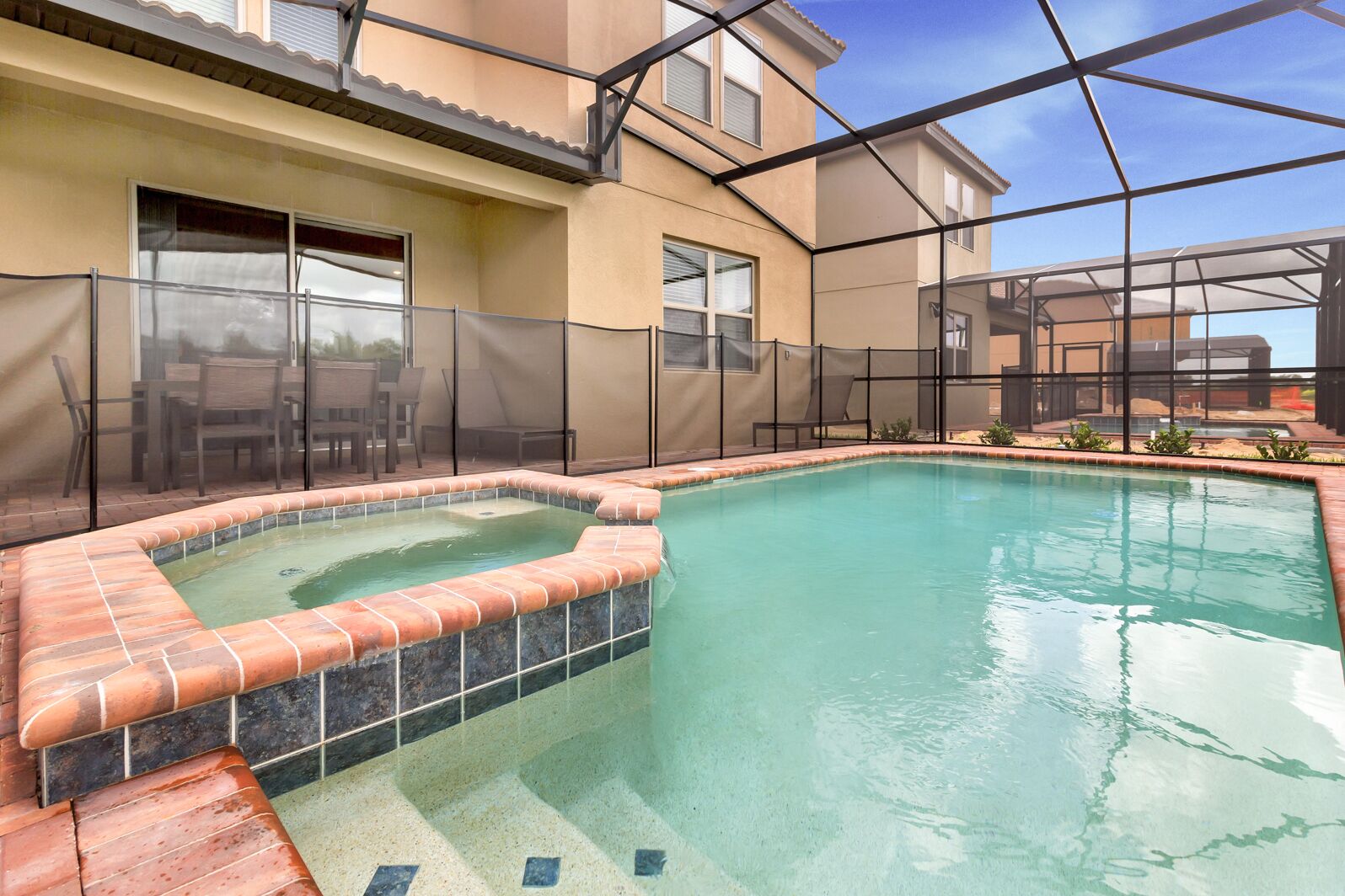 A swimming pool with a hot tub, surrounded by a fence and a patio area with chairs.