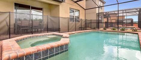 A swimming pool with a hot tub, surrounded by a fence and a patio area with chairs.